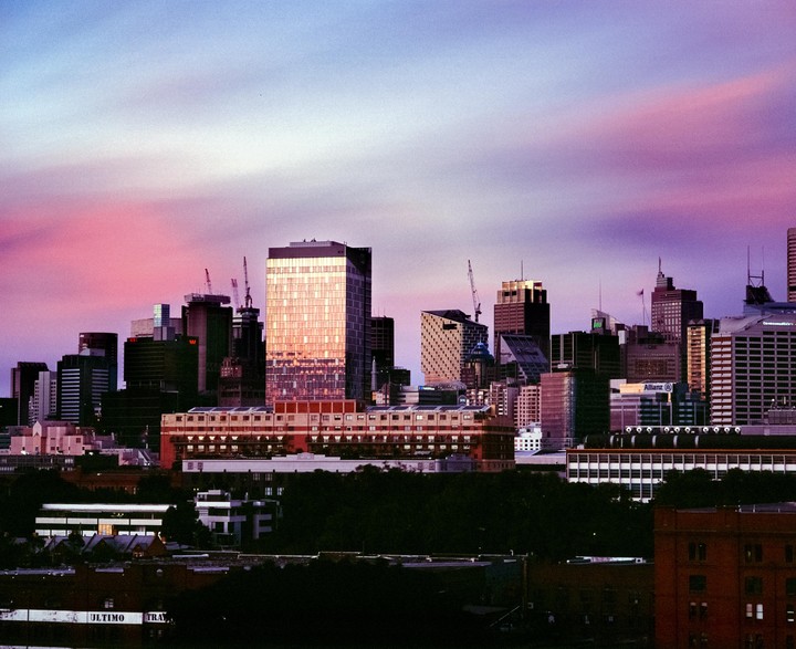 A cityscape with many buildings is visible under a colorful sky at dusk.