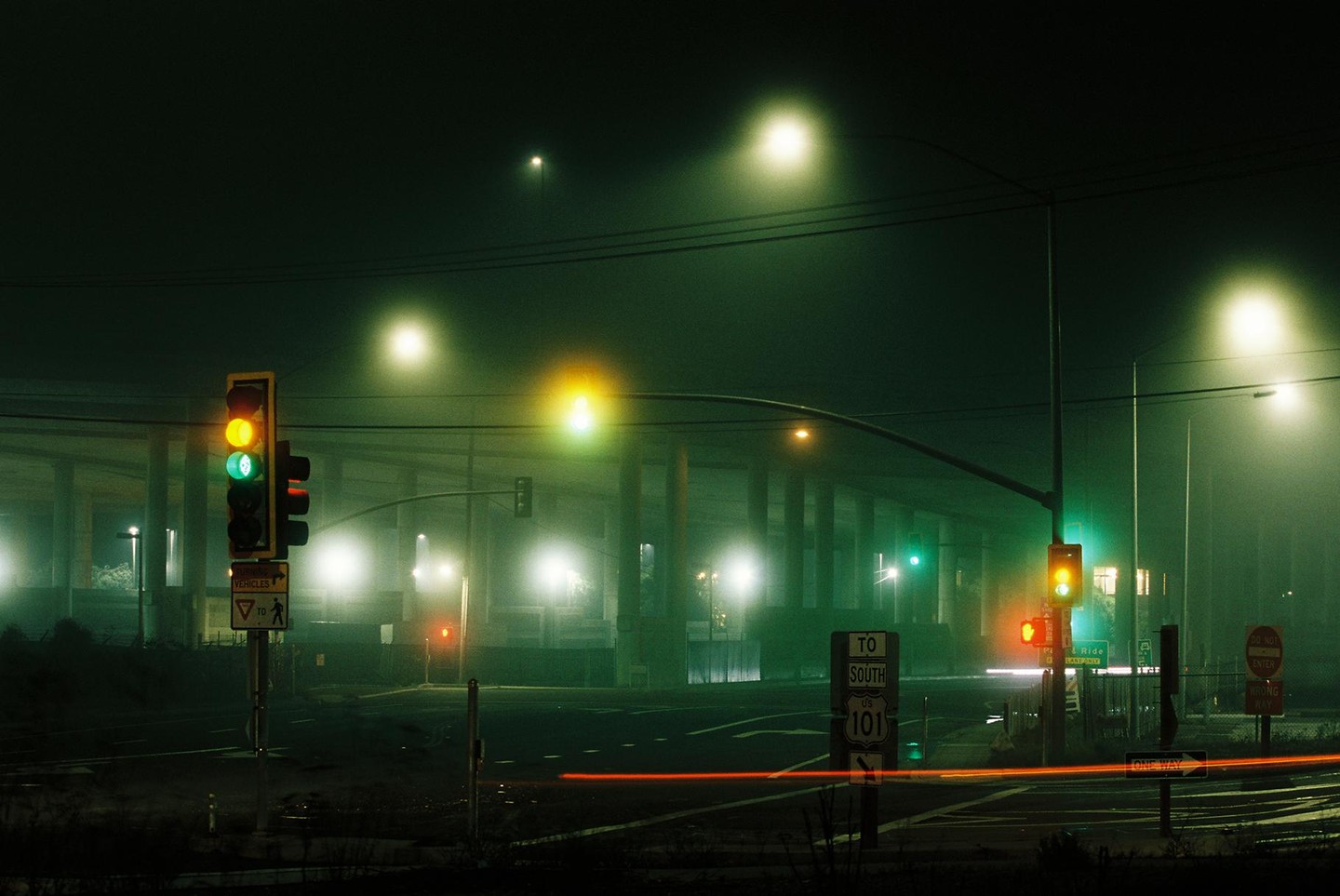 A foggy night scene shows a street with traffic lights and a highway overpass in the background.