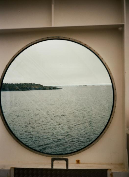A view of the ocean and a tree-covered island is seen through a ship's porthole.