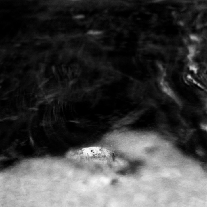 A single white rock is partially submerged in dark, swirling water.