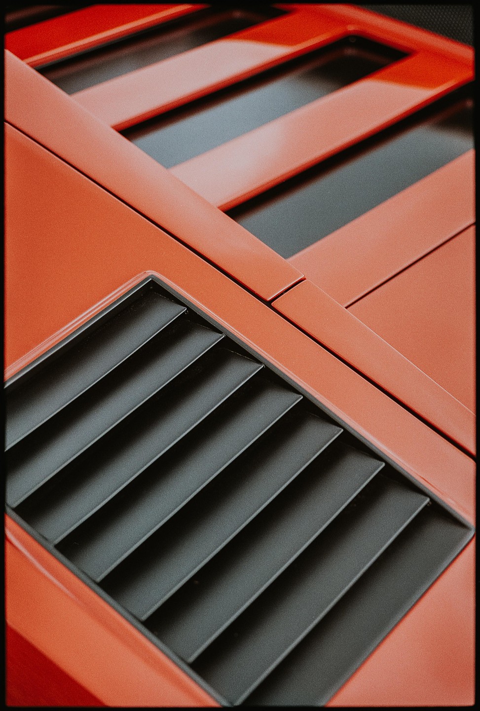A close-up abstract view of the orange bodywork and black vents of a Lamborghini Countach.