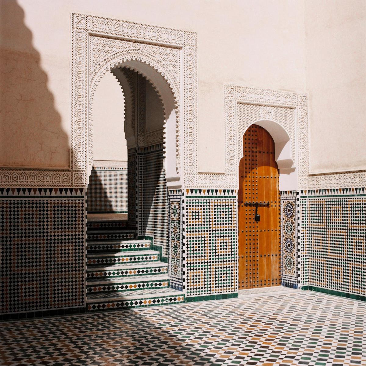 A tiled courtyard features an arched doorway, a wooden door, and a staircase.