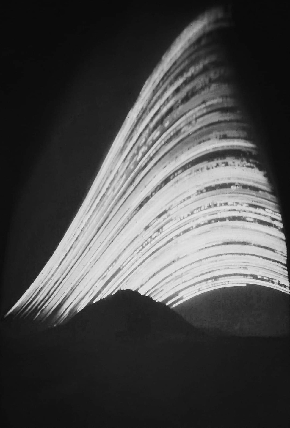 Light trails from stars arc over a mountain peak in a long exposure.