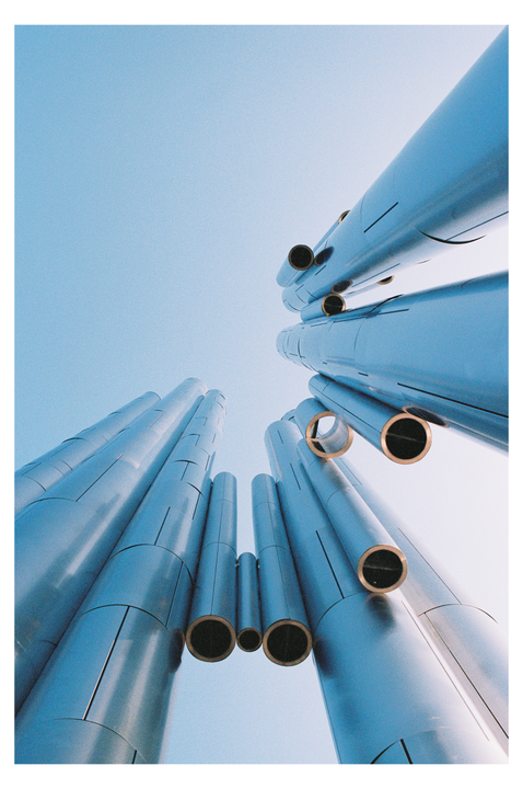 A low-angle view shows a cluster of metallic pipes against a clear blue sky.