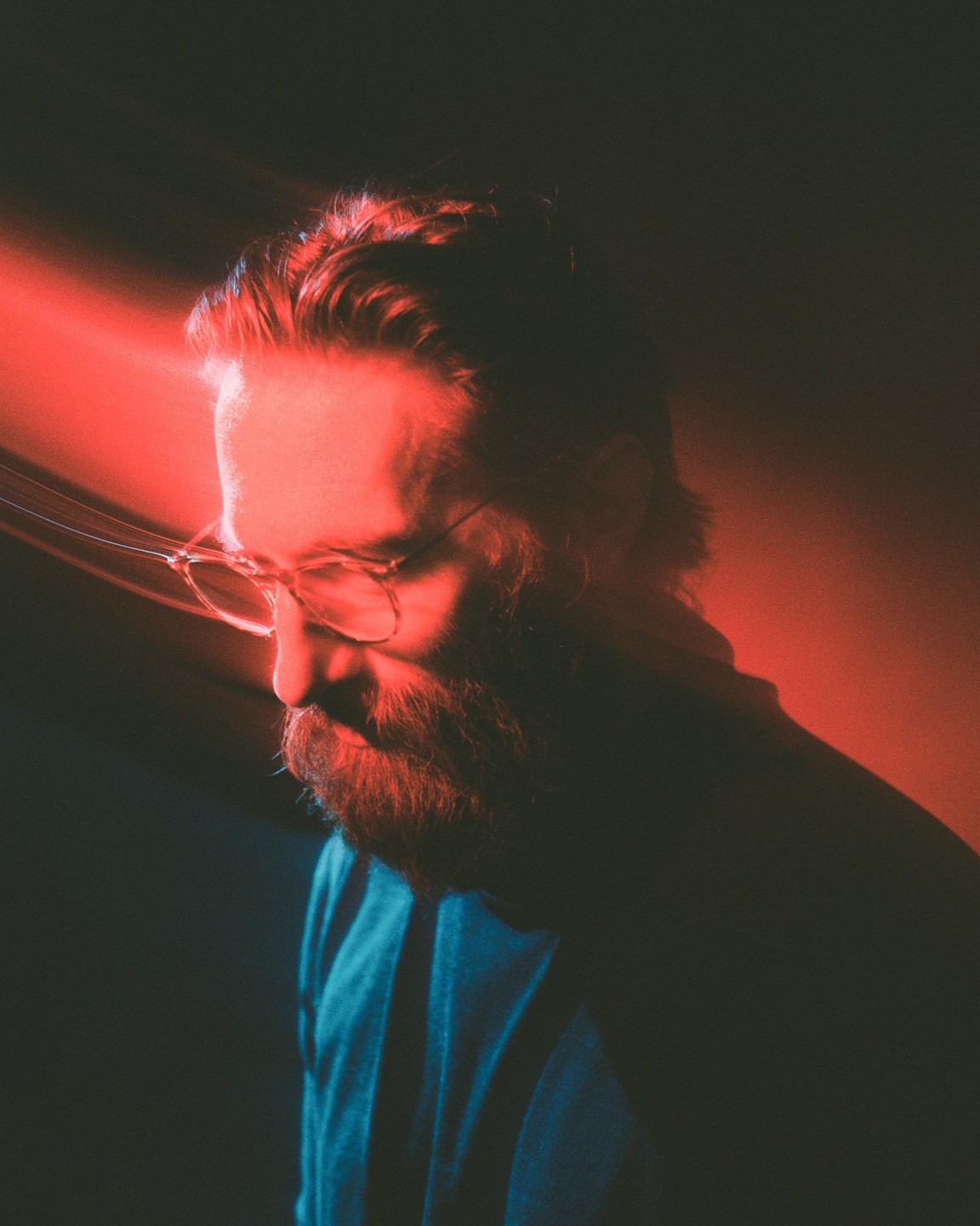 A man with a beard and glasses is illuminated by red and blue light.