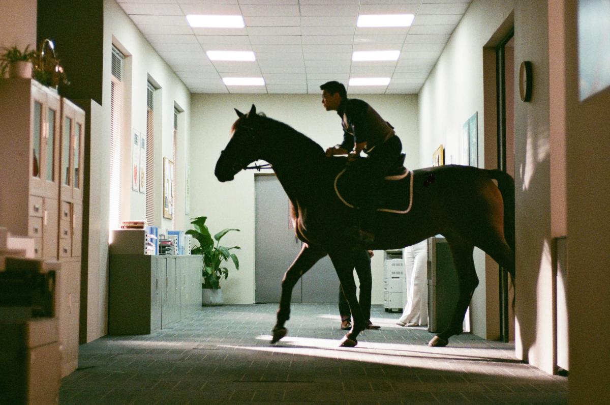 A man rides a horse down a brightly lit office hallway.