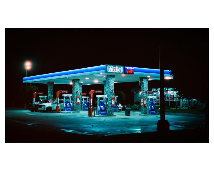A Mobil gas station is illuminated at night with a car parked at one of the pumps.