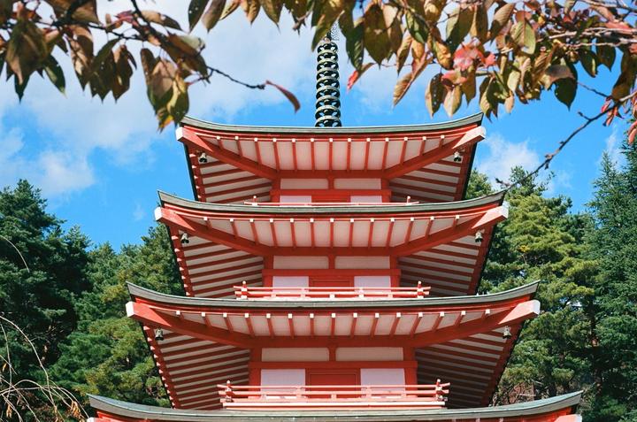 A red pagoda stands tall against a blue sky, surrounded by green trees and framed by autumn leaves.