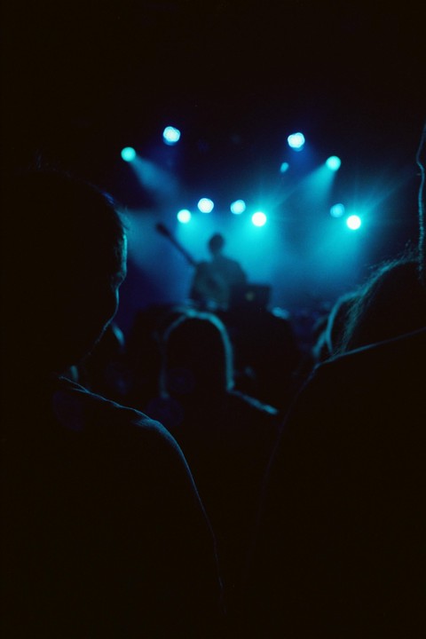 A crowd watches a musician on stage illuminated by blue lights.