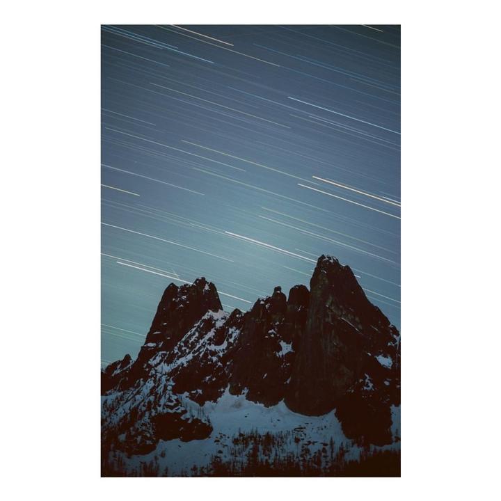 Snow-covered mountains are visible under a night sky with star trails.
