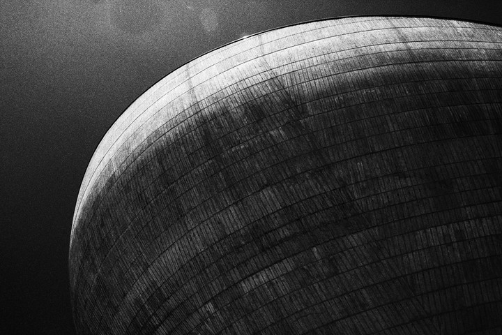 A large, curved, textured building is shown against a dark sky.