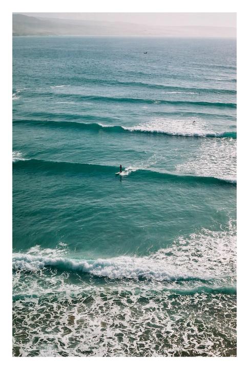 A surfer rides a wave in the ocean with mountains in the distance.
