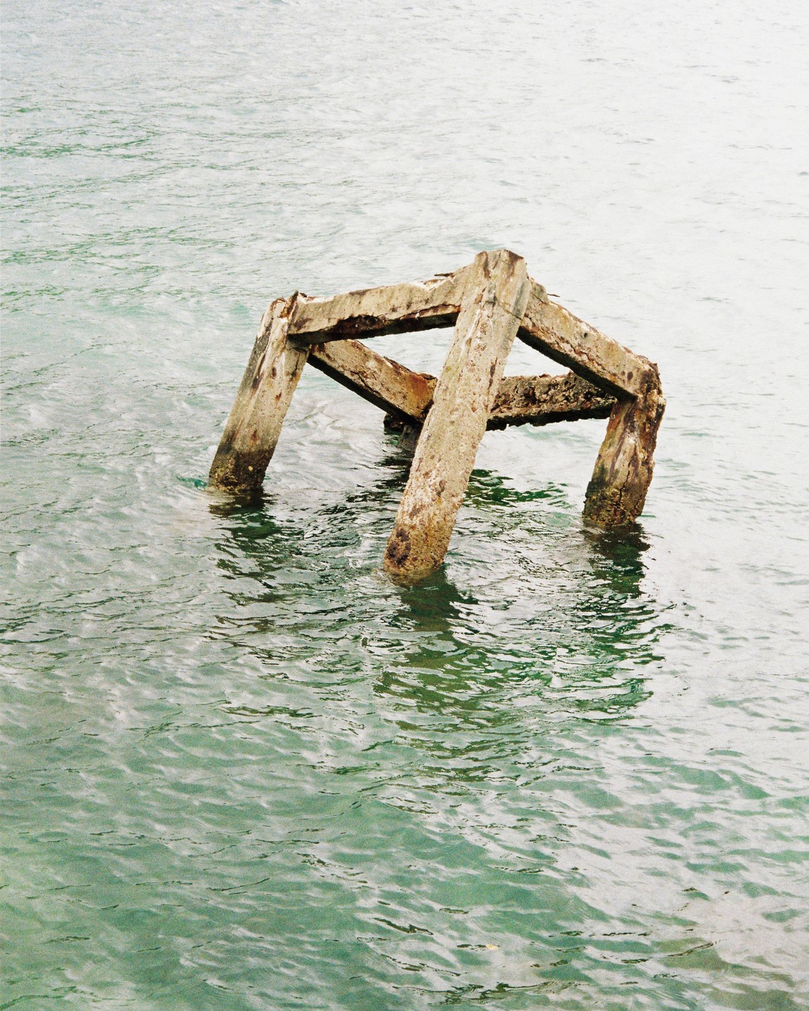 A concrete structure resembling a cube is partially submerged in calm water.
