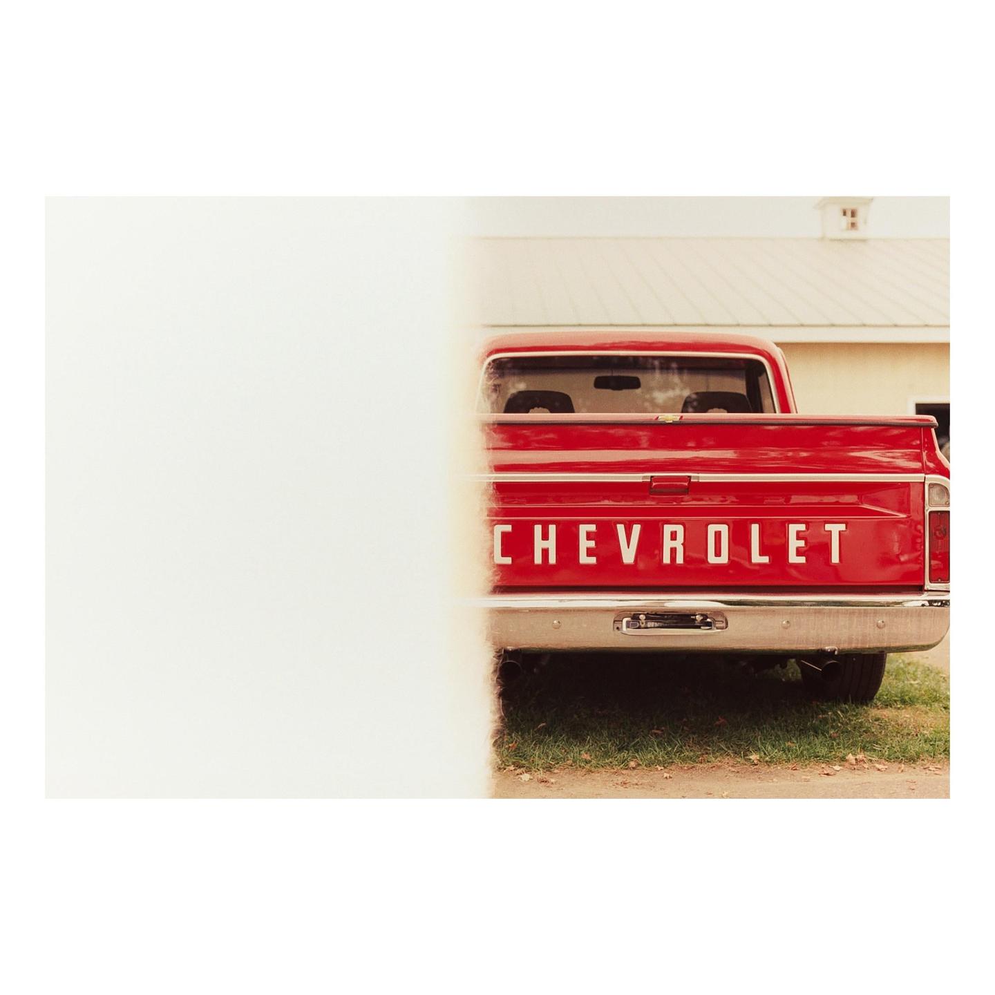 The back of a red Chevrolet pickup truck is partially obscured by a white wall.