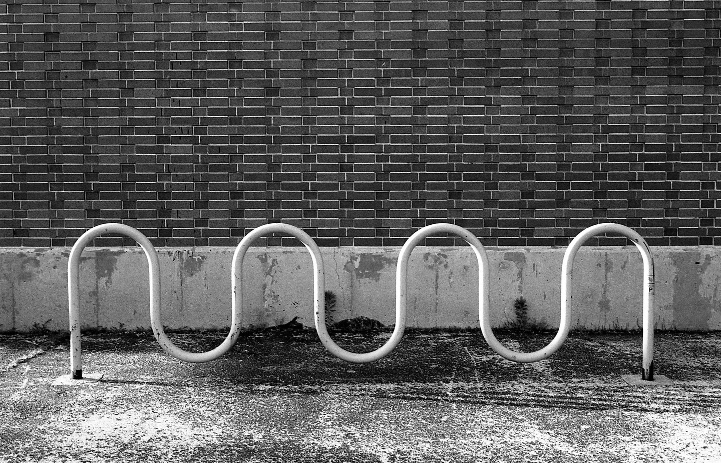 A wavy metal bike rack stands in front of a brick wall and concrete ledge.