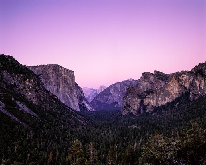 A valley with a forest and mountains is visible under a purple sky.