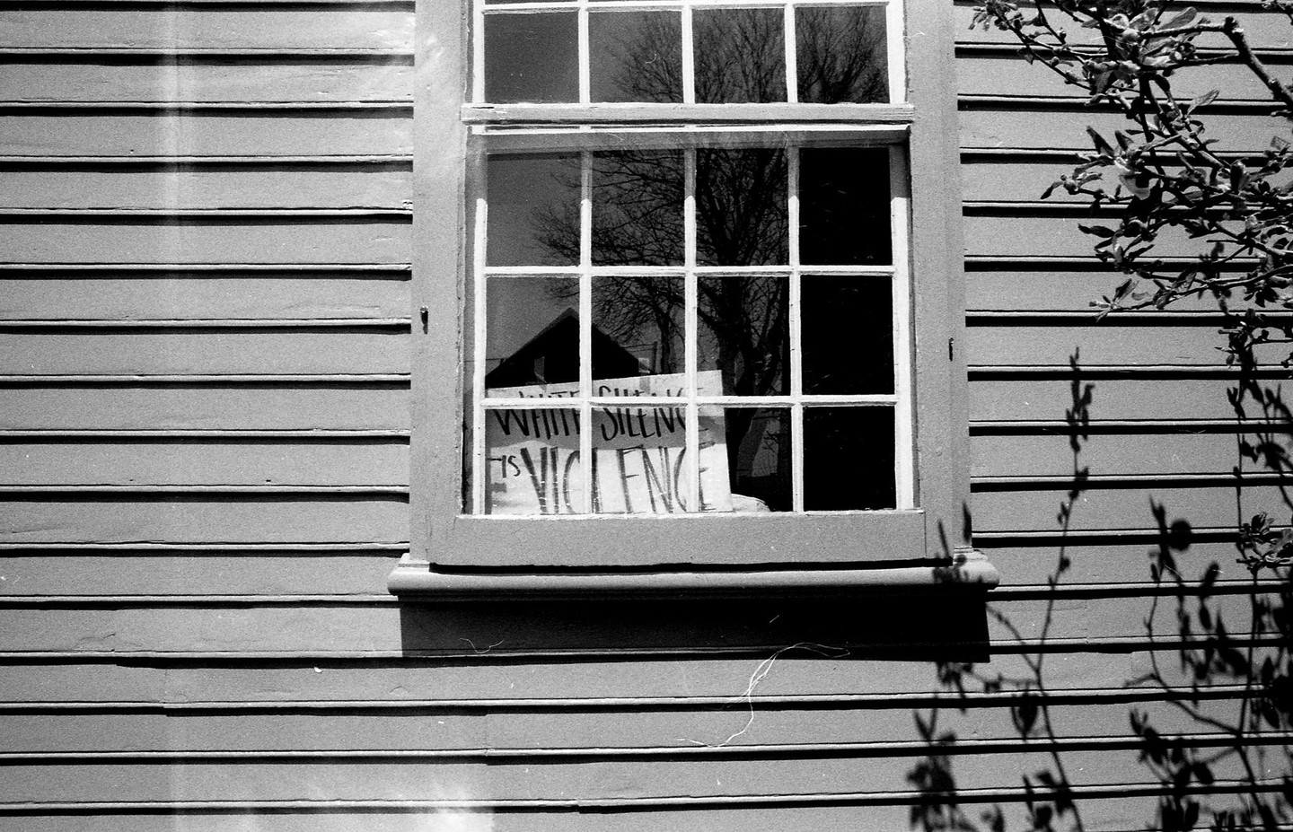 A sign that reads "White Silence is Violence" is visible through a window on a building with horizontal siding.