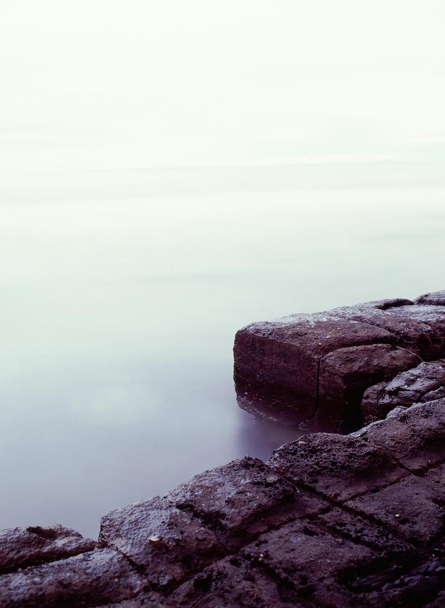 A long exposure captures the smooth surface of the ocean next to dark, textured rocks.
