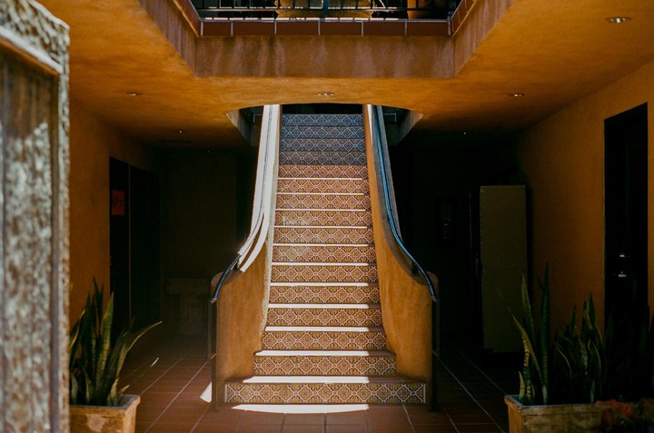 A tiled staircase with a dark blue handrail leads up to a second story in a building with orange walls.
