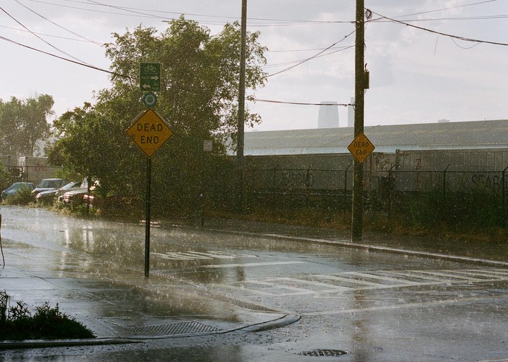 A street is wet from a torrential downpour with two dead end signs and a distant building.