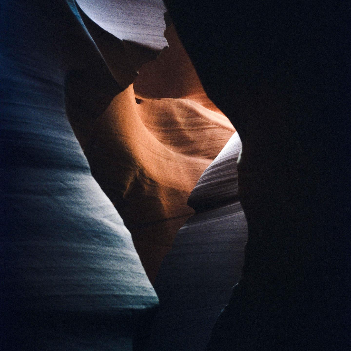 Light illuminates the orange and blue rock formations of a slot canyon.