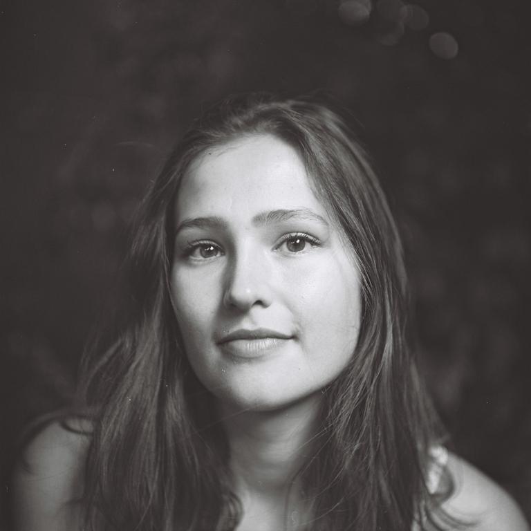 A young woman with long hair looks directly at the viewer.