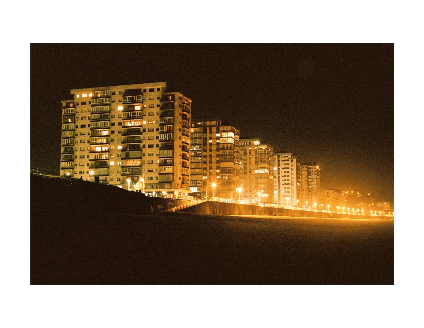 A row of illuminated buildings stands along a dark beach at night.