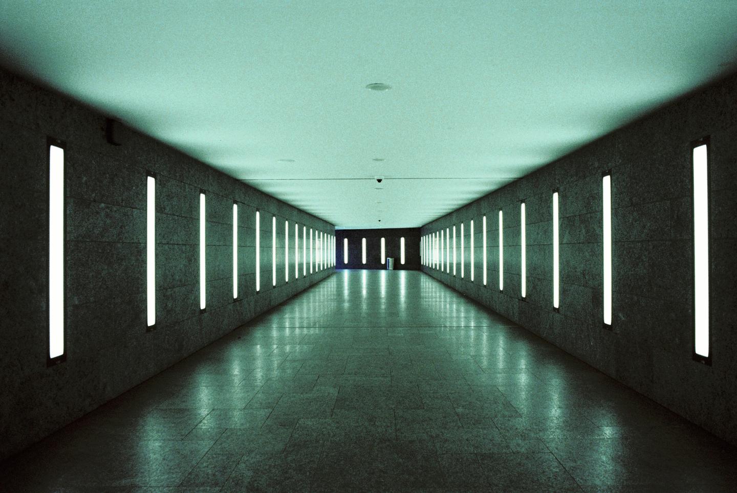 A long, empty subway tunnel is illuminated by vertical fluorescent lights on both walls.