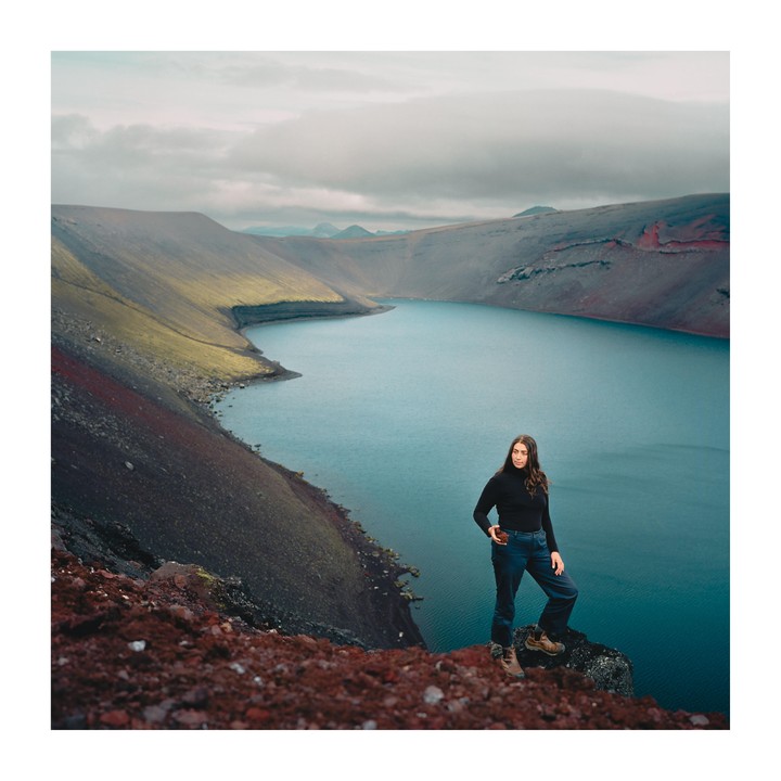 A woman stands on a rocky outcrop overlooking a lake surrounded by mountains.