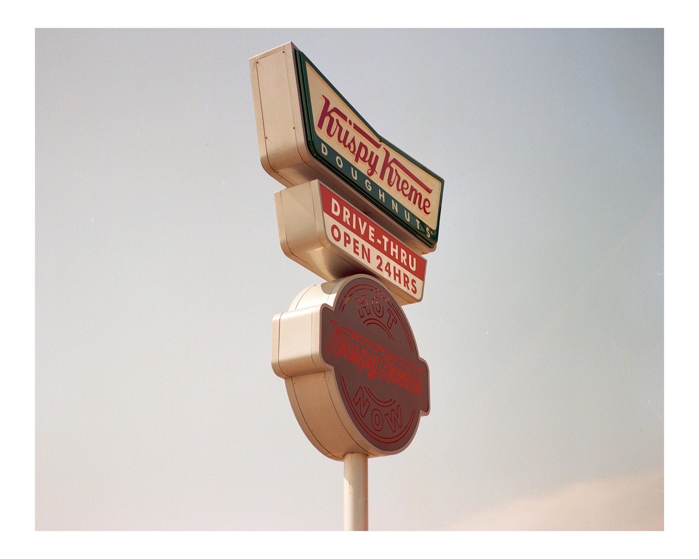 A Krispy Kreme sign with a "Hot Now" light is visible against a clear sky.