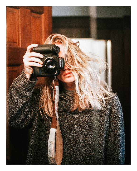 A person with long blonde hair takes a self-portrait with a camera.