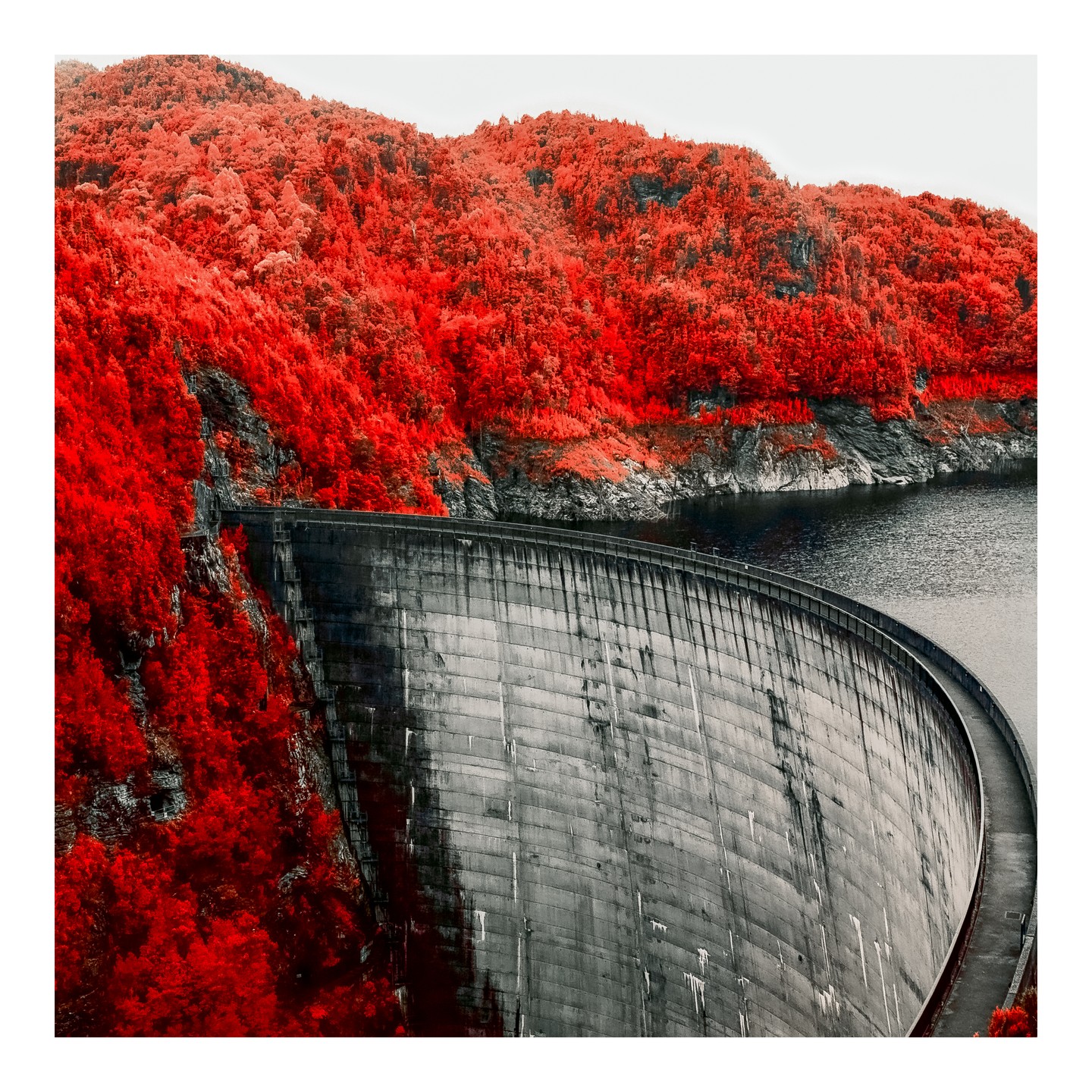 A large concrete dam curves around a body of water, with a mountain covered in red foliage in the background.