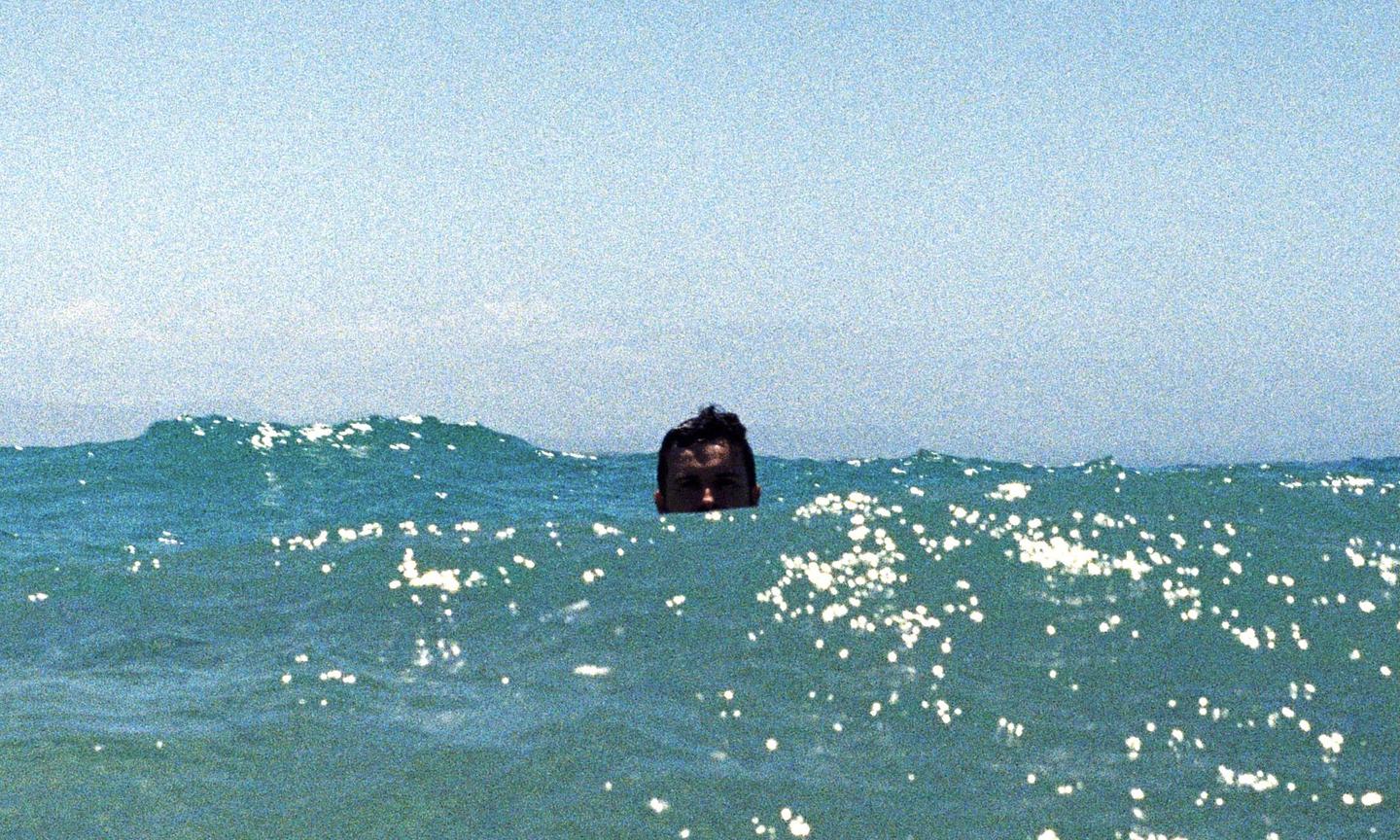A man's head is visible above the surface of the ocean with sparkling water.