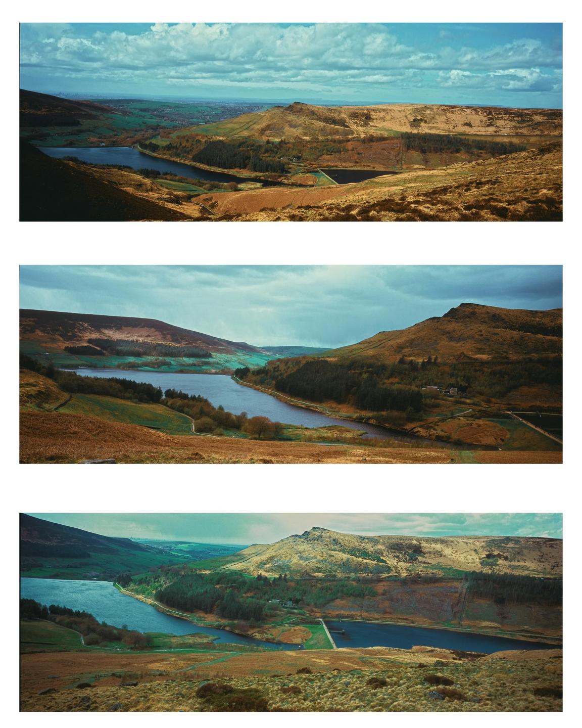 A panoramic landscape shows a reservoir nestled between rolling hills under a cloudy sky.