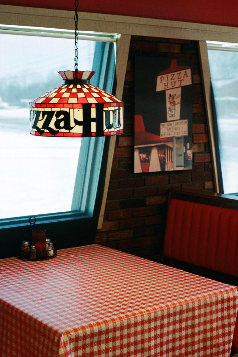A red and white checkered Pizza Hut lamp hangs above a matching tablecloth and red booth seating.