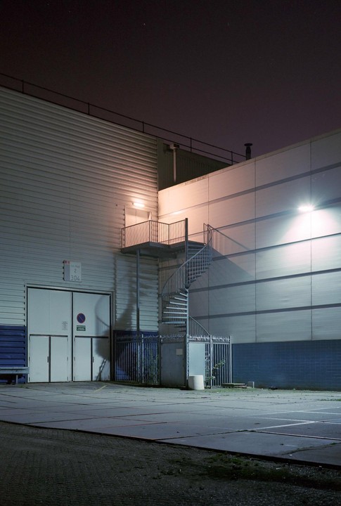 A spiral staircase leads up to a door on the side of a building at night.
