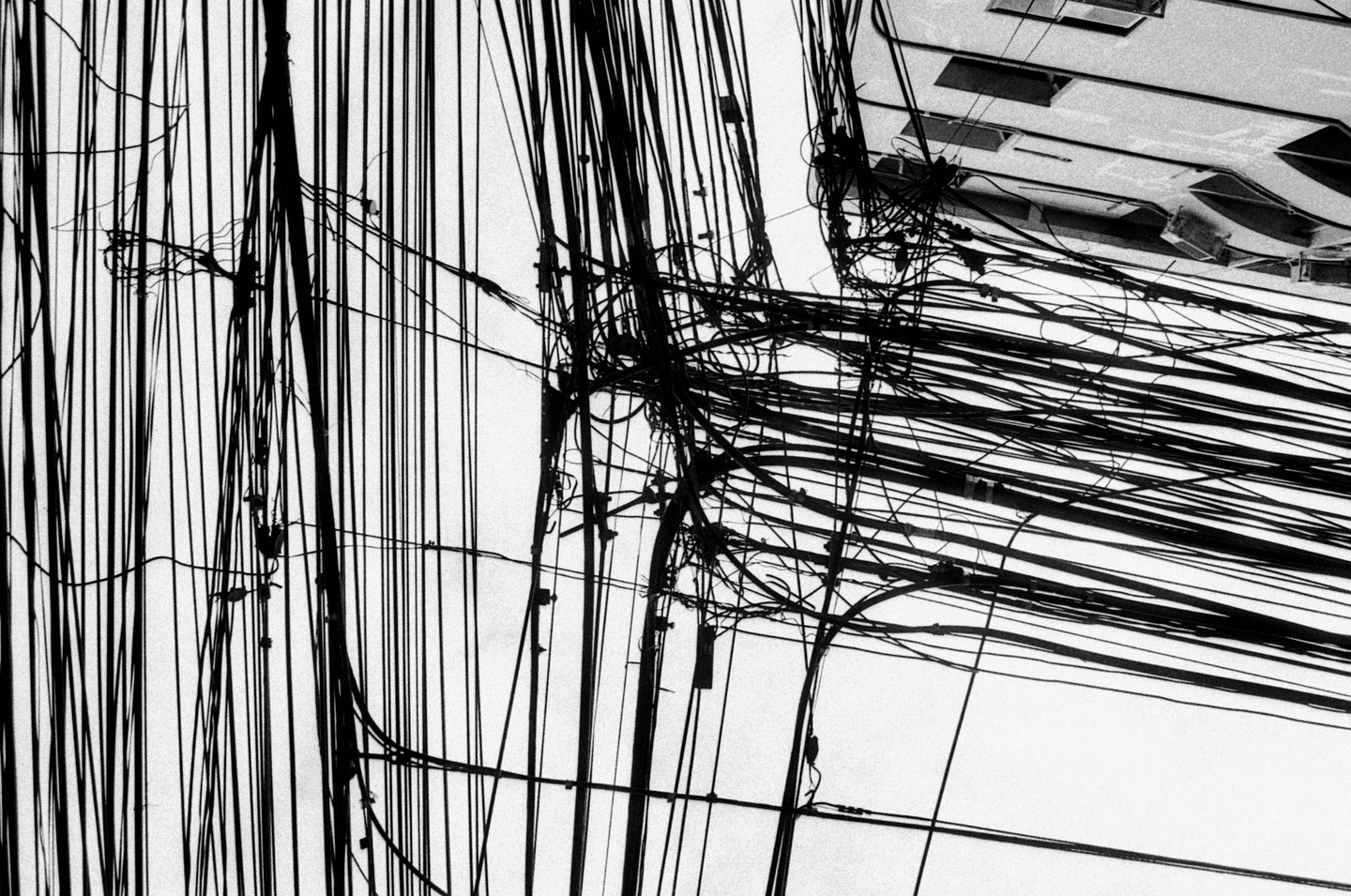 A dense network of overhead power lines and communication cables crisscrosses against a bright sky, with a building visible in the upper right.