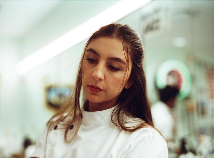 A woman in a white chef's coat looks down with a soft expression.