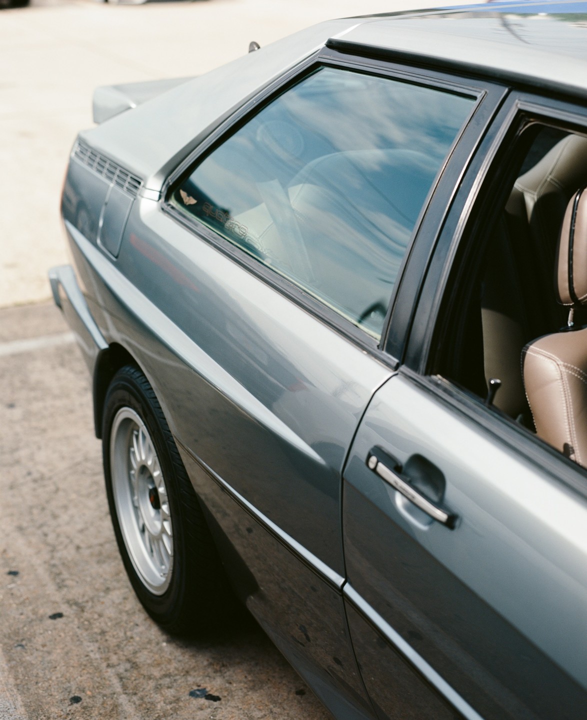 A gray car with a brown interior is parked on a concrete surface.