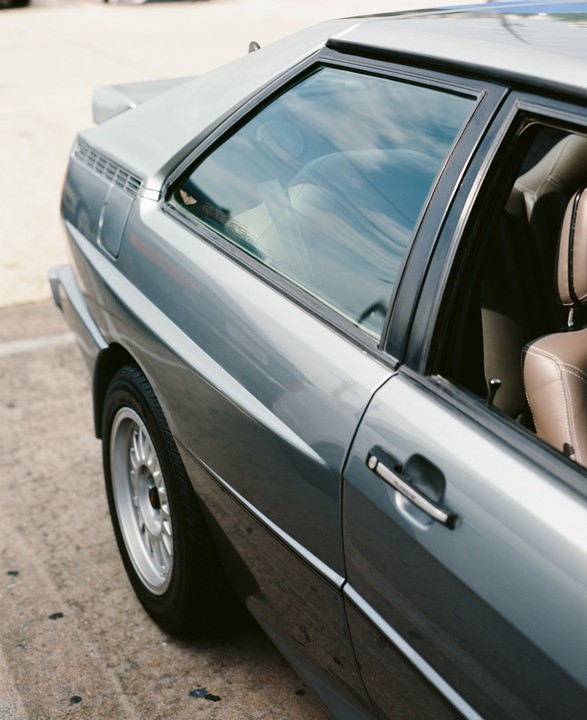 A gray car with a brown interior is parked on a concrete surface.