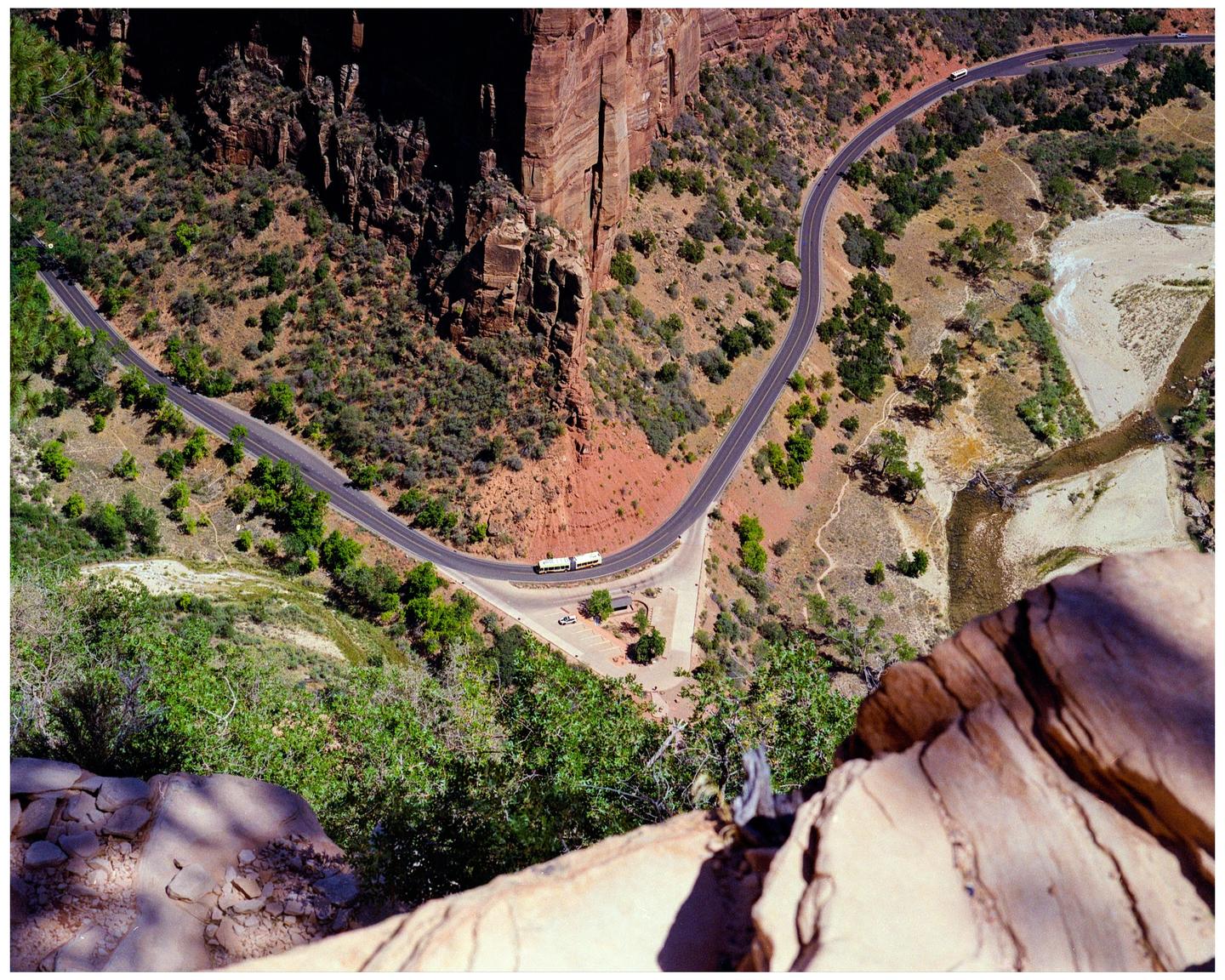 A winding road with two buses on it is visible from a high vantage point overlooking a canyon.