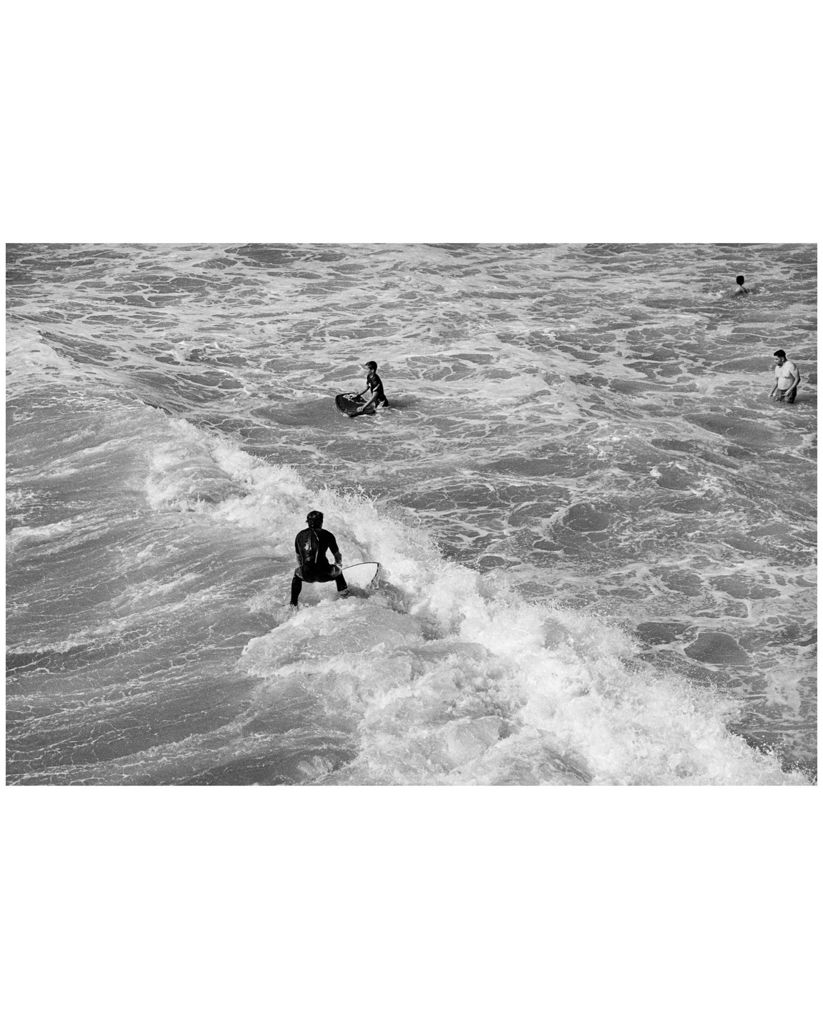 A surfer rides a wave while other people are in the ocean at Manhattan Beach.