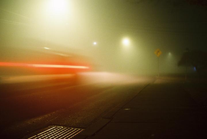 A street at night is illuminated by streetlights and the red light trails of a passing vehicle.