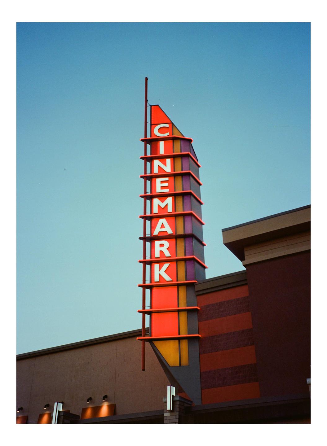 A tall, colorful Cinemark sign stands against a clear blue sky next to a building.