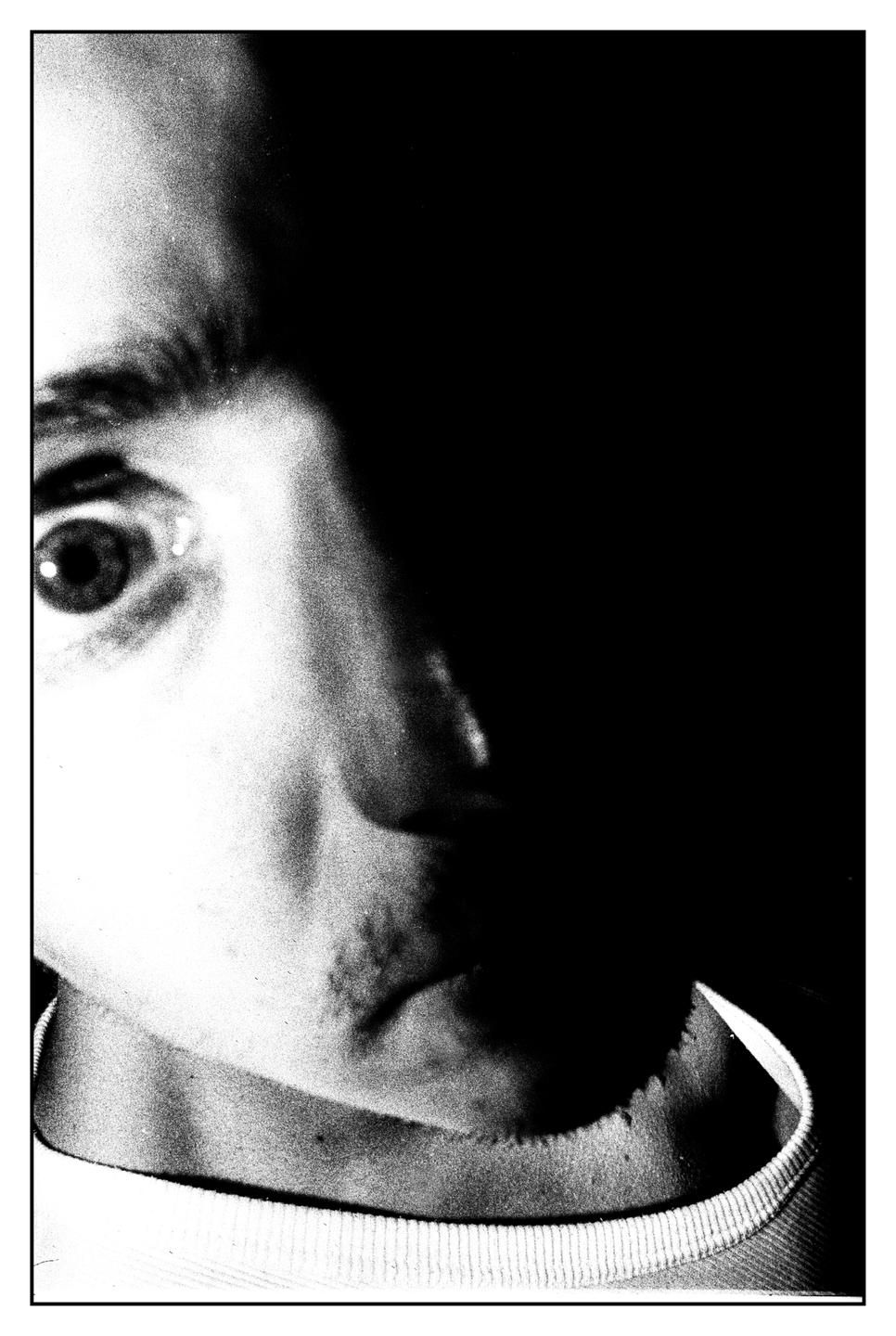 A man's face is partially illuminated in a high-contrast black and white portrait.