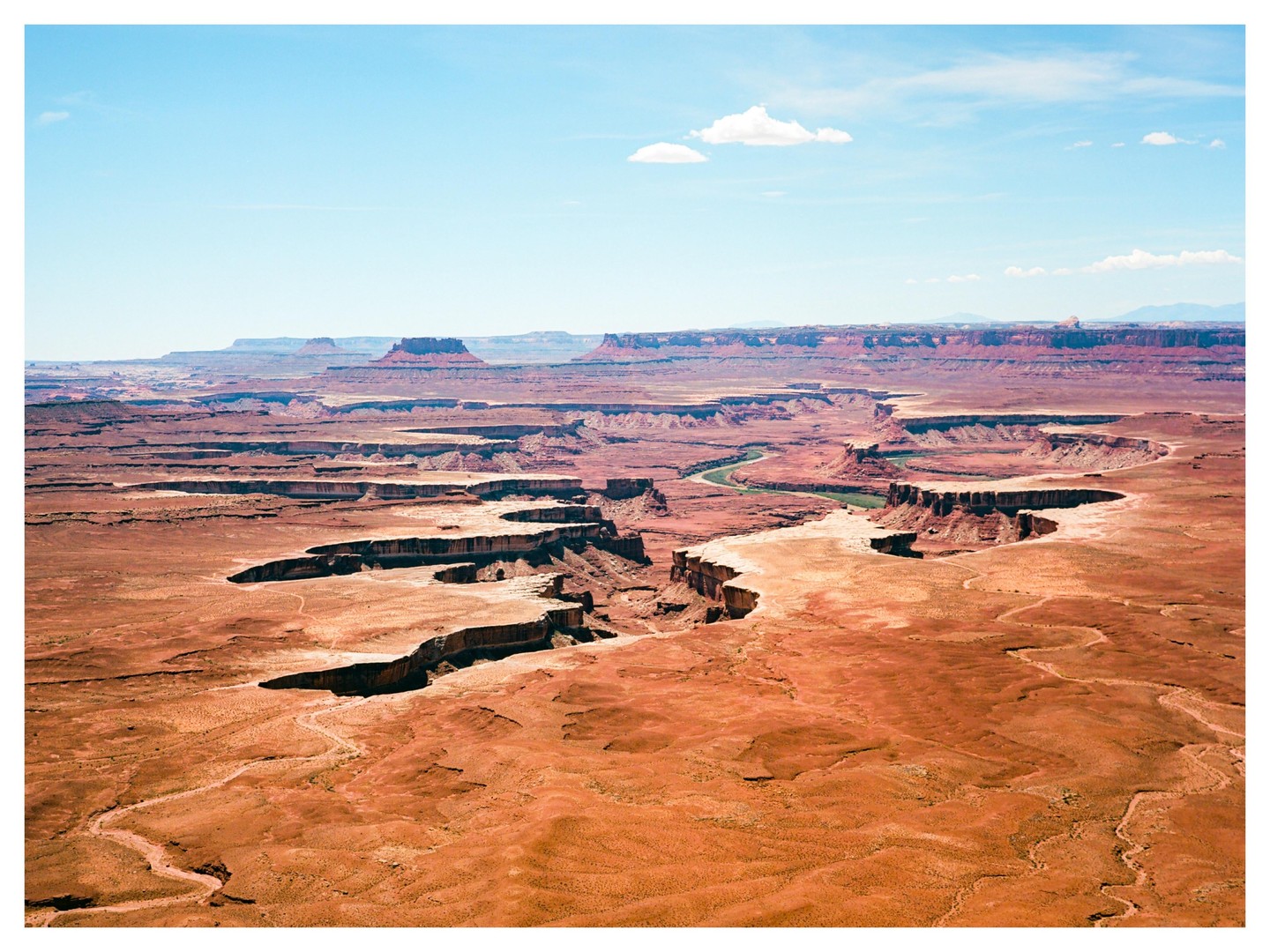 A wide shot shows a winding river through a vast canyon landscape under a blue sky with a few clouds.