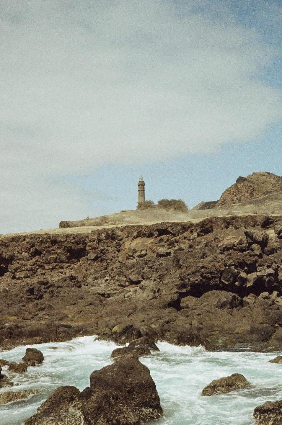A lighthouse stands on a rocky cliff overlooking the ocean with waves crashing against the shore.