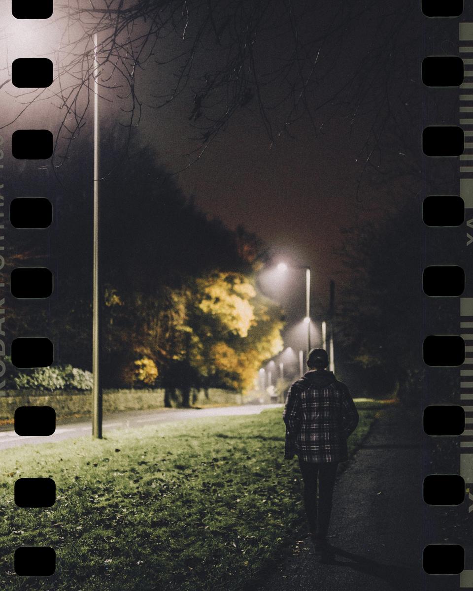 A person walks along a path at night, illuminated by streetlights.