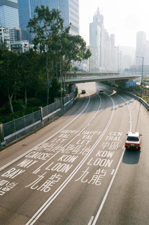 A multi-lane highway with cars and an overpass is surrounded by tall buildings and trees.