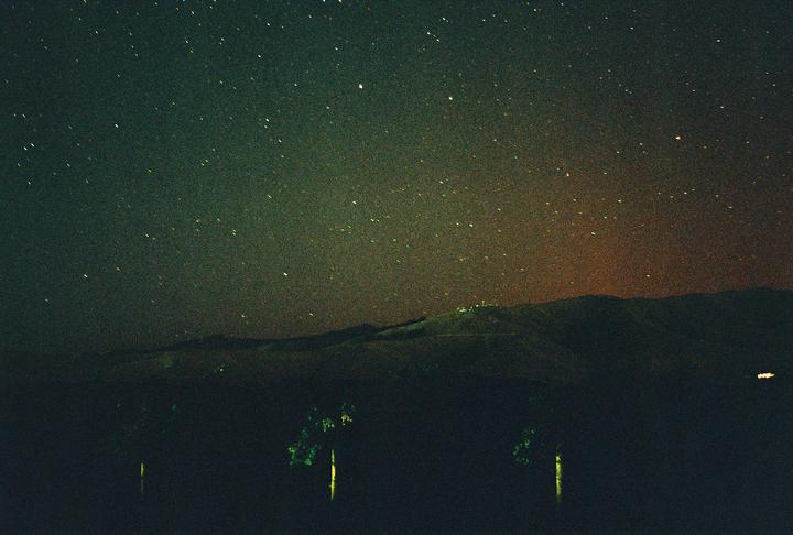A starry night sky with a faint aurora glow is visible above a dark landscape with hills and trees.